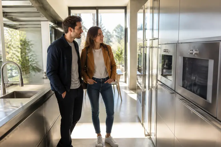 Un couple français admire une cuisine moderne avec des finitions en acier galvanisé ou inox.