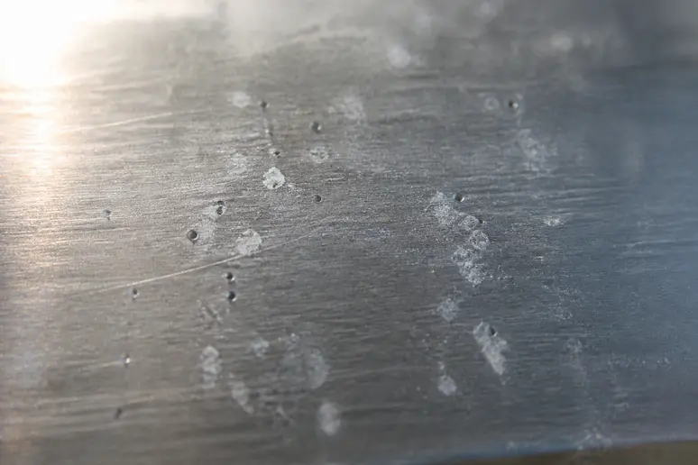 Gros plan sur des piqûres d'oxydation et un voile blanc sur une pièce en aluminium.
