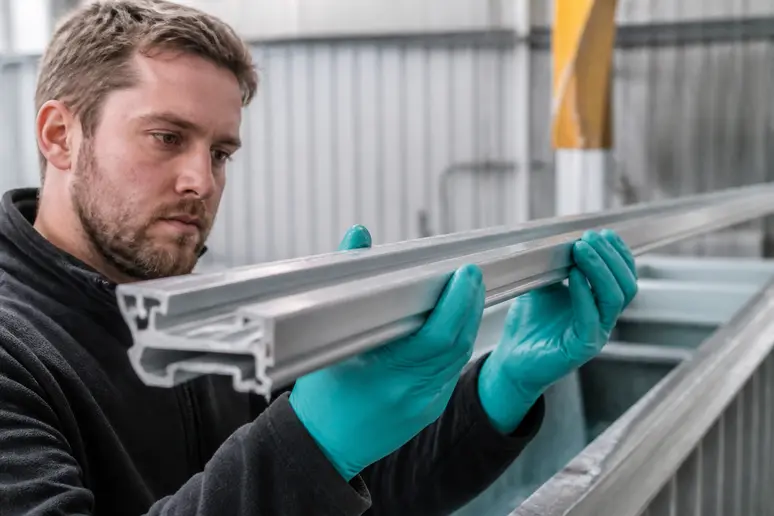 Contrôle visuel d'un profilé en aluminium avant le traitement de thermolaquage en atelier.