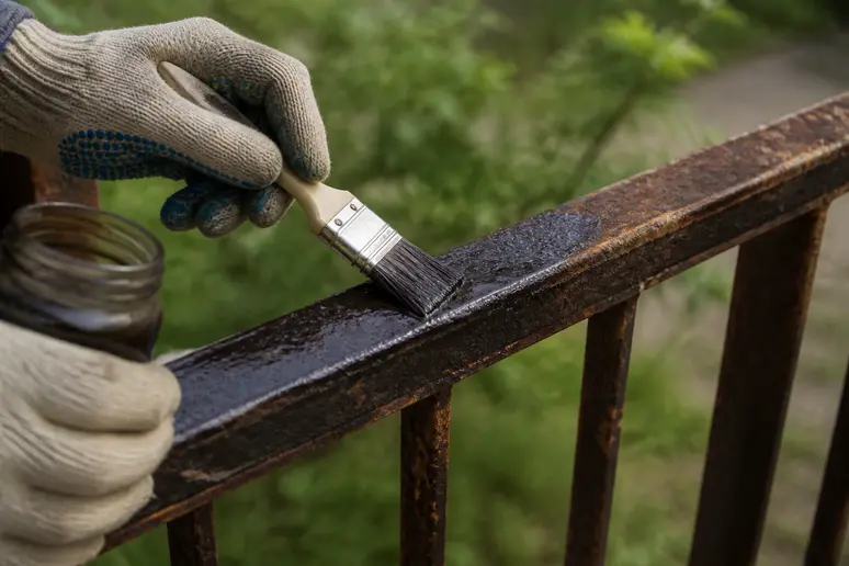Application d'un traitement antirouille au pinceau sur une ferronnerie extérieure oxydée avant la peinture.