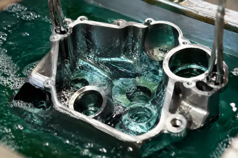 Pièce mécanique complexe immergée dans un bain de nickelage chimique pour un dépôt uniforme.
