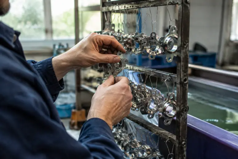 Technicien fixant des pièces métalliques sur une attache pour un traitement de nickelage soigné.