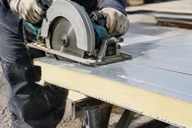 Découpe minutieuse d'un panneau sandwich de bac acier isolé sur un chantier de toiture.