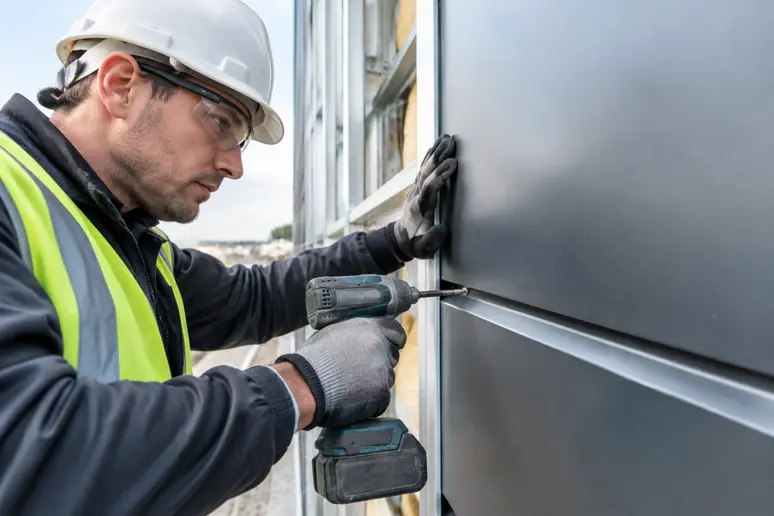 Ouvrier posant un bardage métallique avec précision sur un chantier de façade.